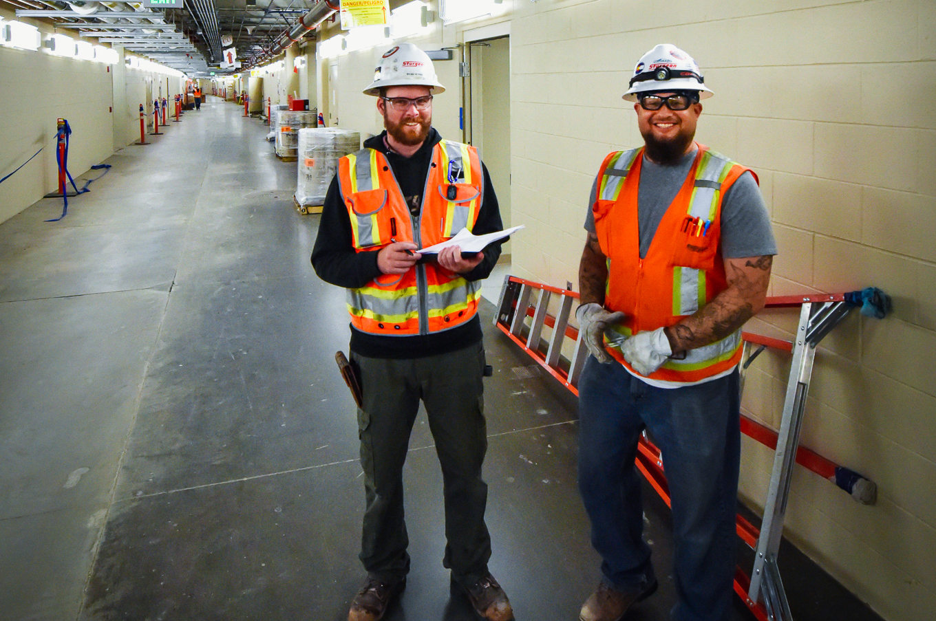 Two Sturgeon Electric employees in a utility hallway smile for the camera